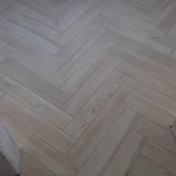 Ułożona pod kątem jasna podłoga z płytek imitujących drewno, widoczny fragment ściany z gniazdkiem elektrycznym.