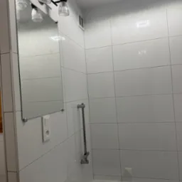 Biała łazienka po remoncie: błyszczące płytki, lustro z oświetleniem i umywalka z baterią. Minimalistyczny design, nowoczesne wykończenie.