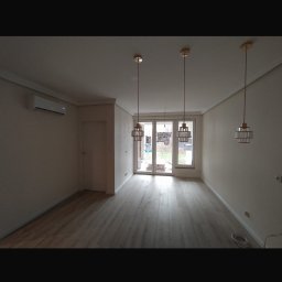 Adnel - Jasne panele podłogowe w przestronnym pokoju z trzema lampami wiszącymi i klimatyzatorem. Świeżo wykończone wnętrze z drzwiami balkonowymi.