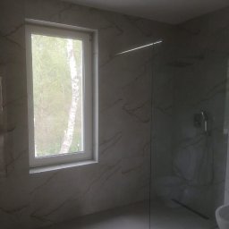 Adnel - Wykończona łazienka z kabiną typu walk-in, płytkami imitującymi marmur na ścianach i podłodze, oraz oknem z widokiem na drzewa. Minimalistyczny design.