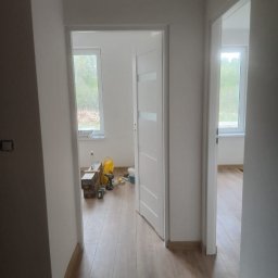 Adnel - Jasne wnętrze po remoncie: świeżo pomalowane ściany, ułożone panele podłogowe, białe drzwi z przeszkleniami. Widoczne narzędzia i materiały malarskie.