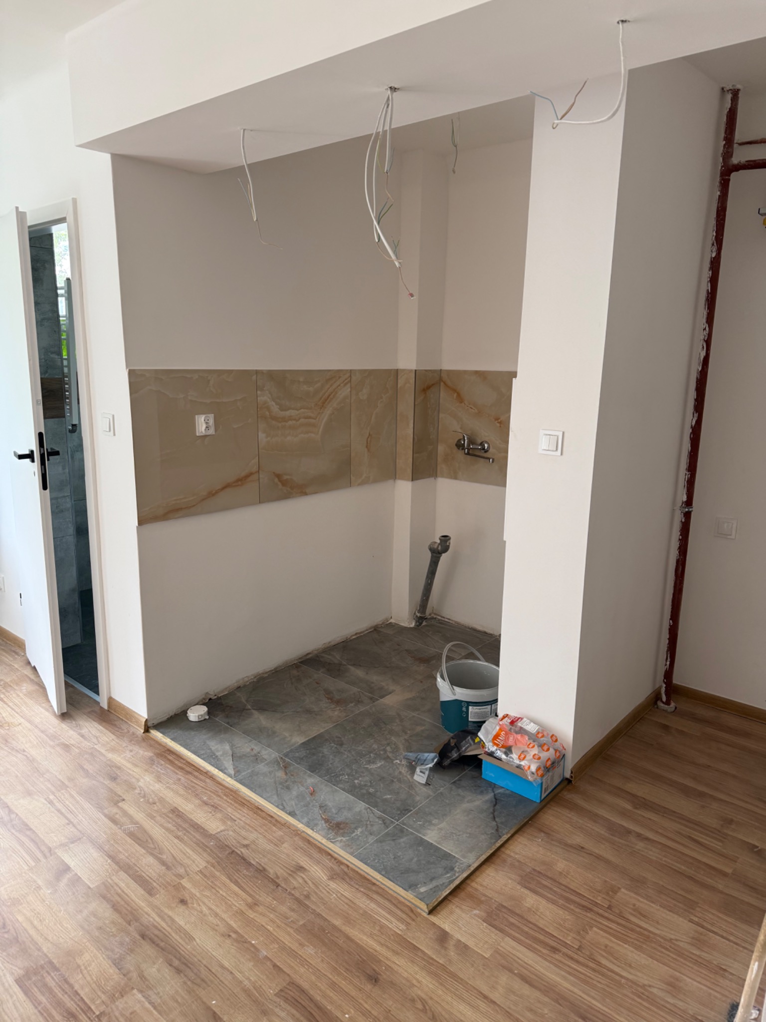 Wnętrze kuchni w trakcie remontu: ułożone płytki podłogowe i ścienne, widoczne przewody, przygotowane materiały. Kontrast płytek i paneli podłogowych.