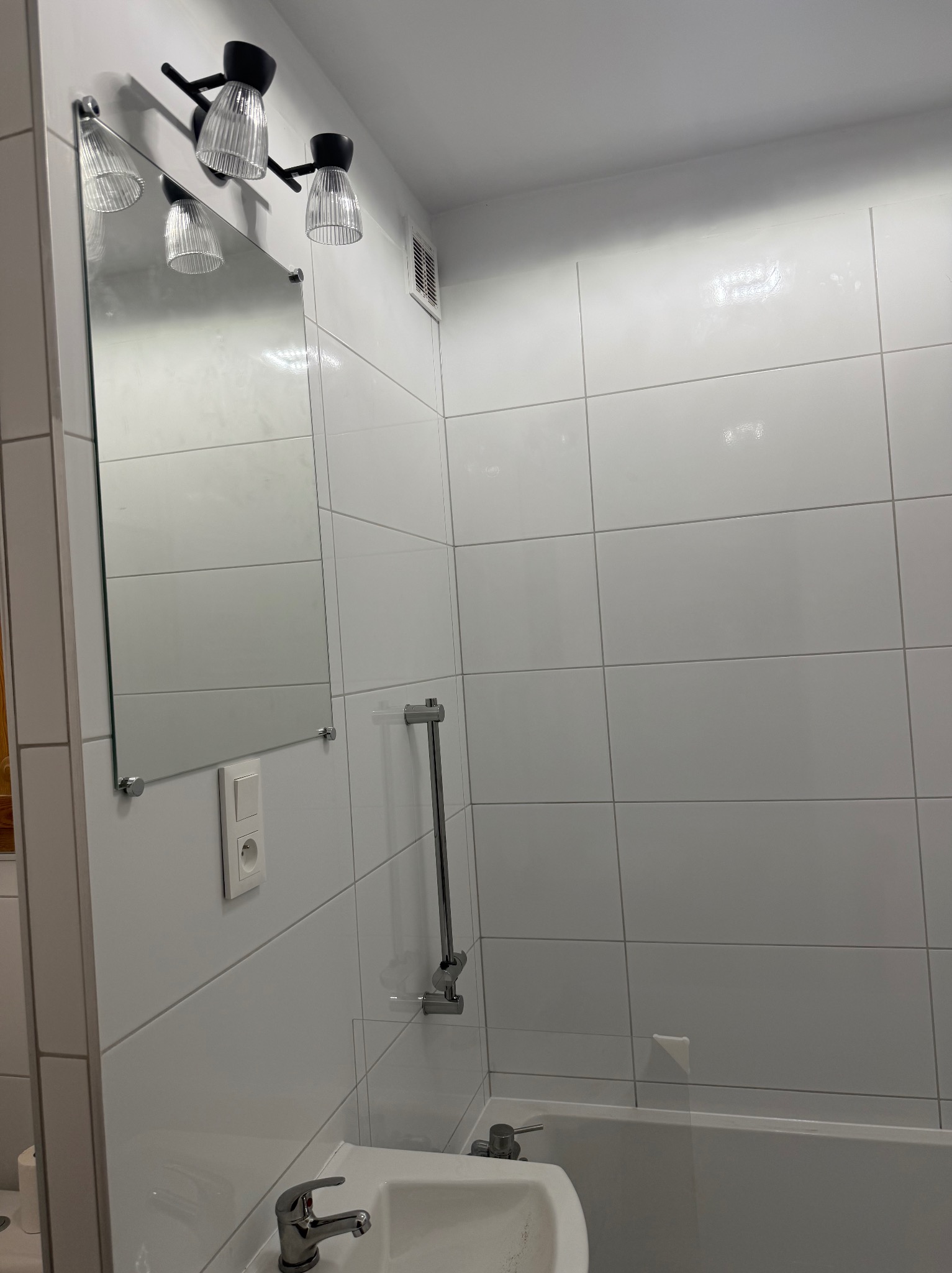 Biała łazienka po remoncie: błyszczące płytki, lustro z oświetleniem i umywalka z baterią. Minimalistyczny design, nowoczesne wykończenie.