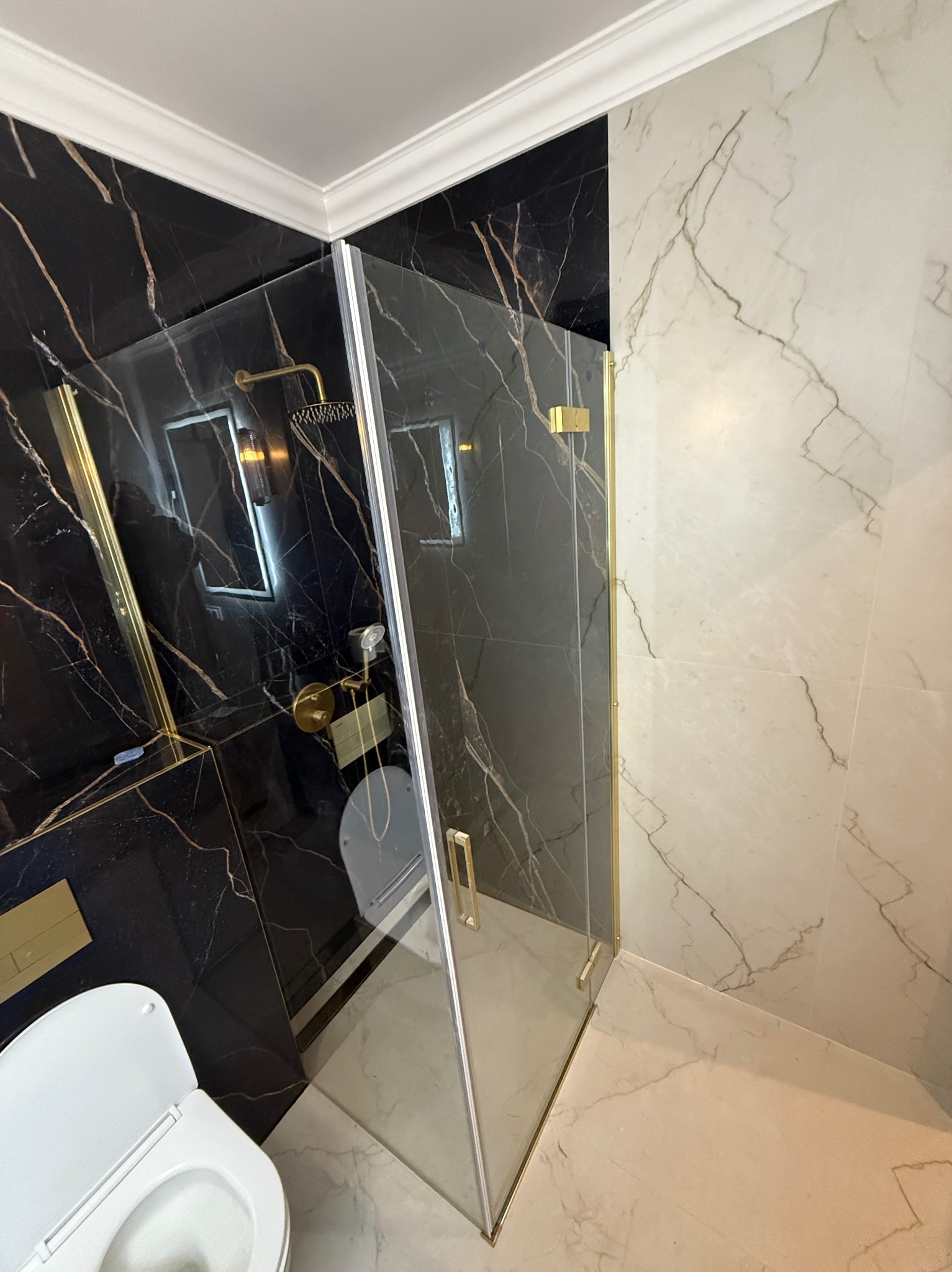 Elegancka kabina prysznicowa z czarnymi i białymi marmurowymi płytkami, złote akcenty, nowoczesny design, widok z góry na toaletę.