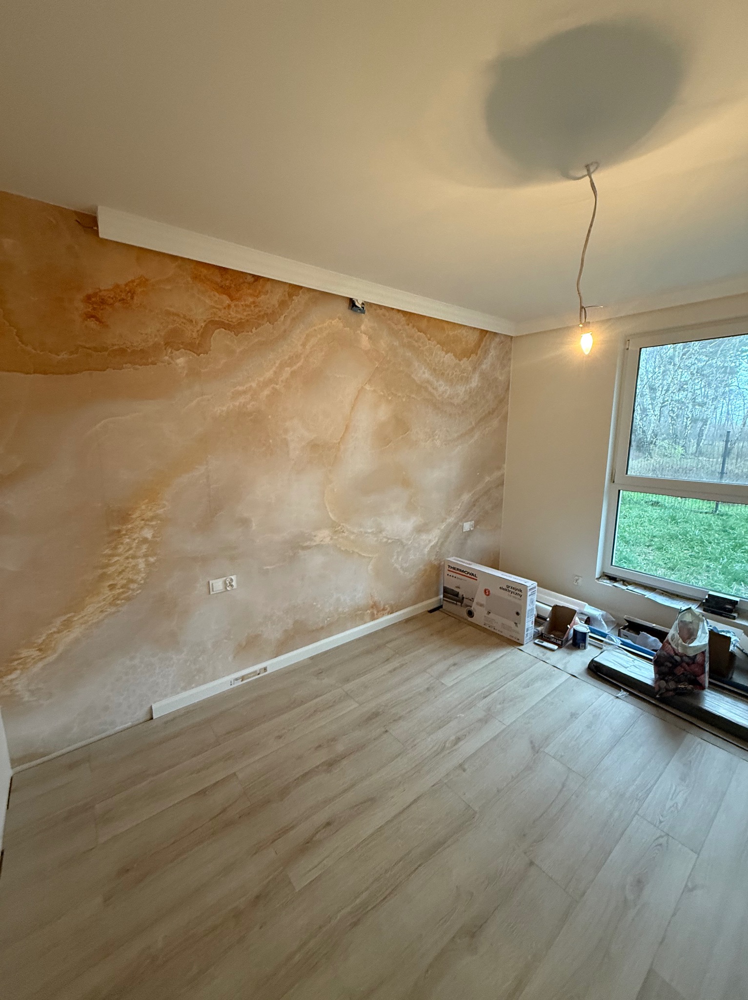 Pokój po wykończeniu: dekoracyjna ściana imitująca marmur, jasna podłoga z paneli, białe listwy przypodłogowe i sufitowe. Widoczne narzędzia i materiały budowlane.