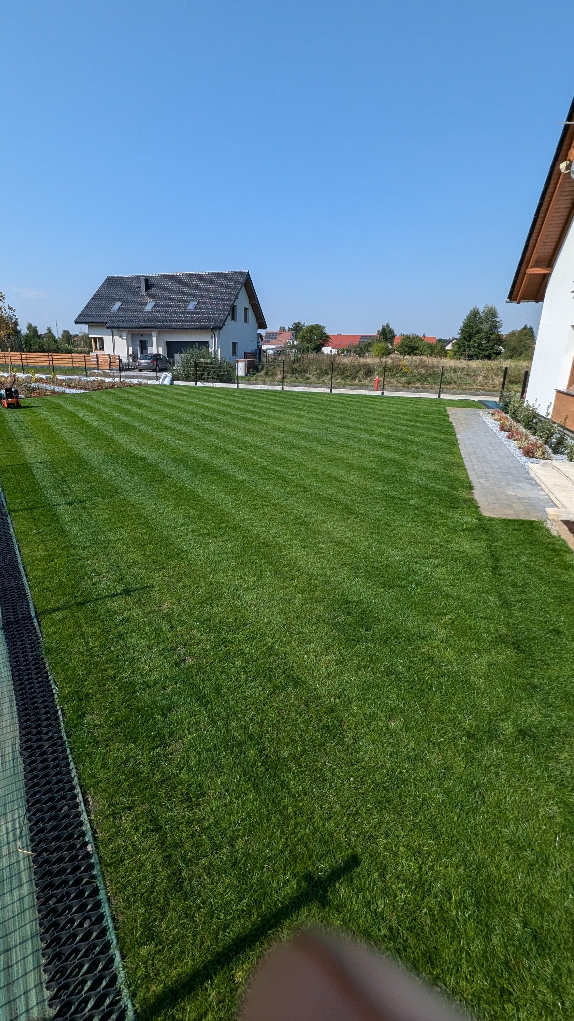 Perfekcyjnie przystrzyżony trawnik w Dobrzeniu Wielkim z widocznymi pasami po kosiarce, zadbany ogród z nowoczesnym domem w tle.