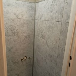 Paweł B - Ściana łazienki wyłożona szarymi płytkami z delikatnym wzorem, widoczne otwory na baterię, ujęcie z bliska.