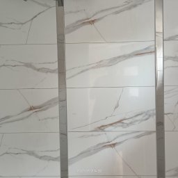 Paweł B - Położone białe płytki imitujące marmur z szarymi i rdzawymi żyłkami, oddzielone srebrnymi listwami, z fragmentem czarnej kurtki w lewym dolnym rogu.