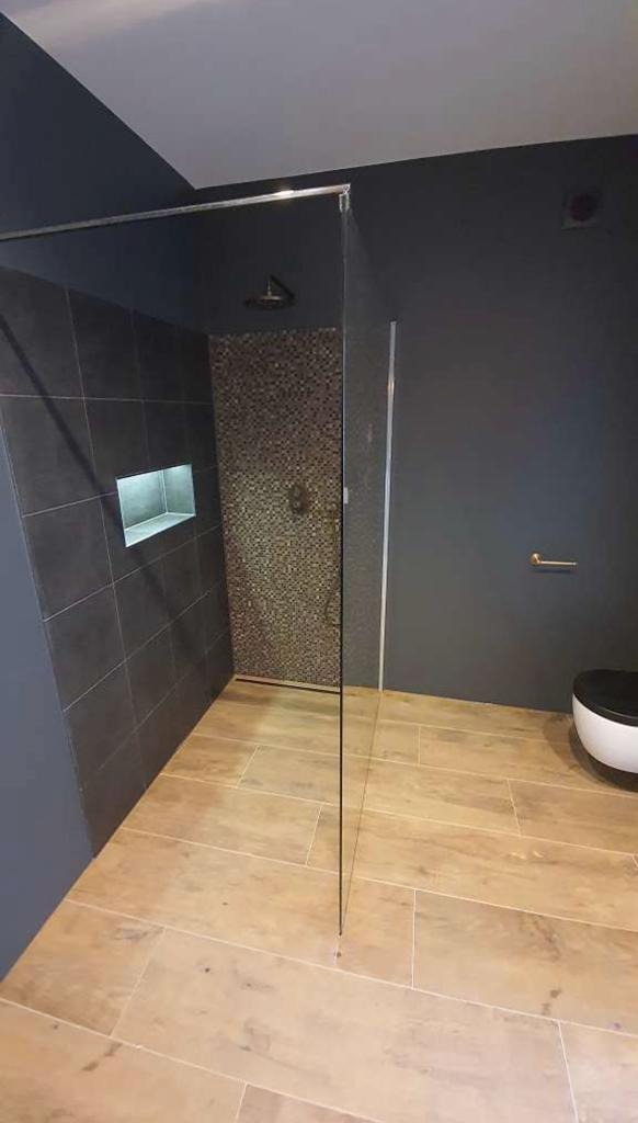 Nowoczesna łazienka z kabiną prysznicową typu walk-in, ciemnoszare płytki ścienne z wnęką, mozaika wewnątrz prysznica i drewnopodobna podłoga.