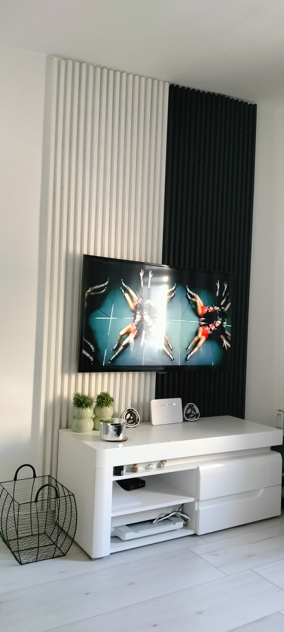 Biało-czarne panele ścienne z pionowymi rowkami za telewizorem na białej szafce RTV.