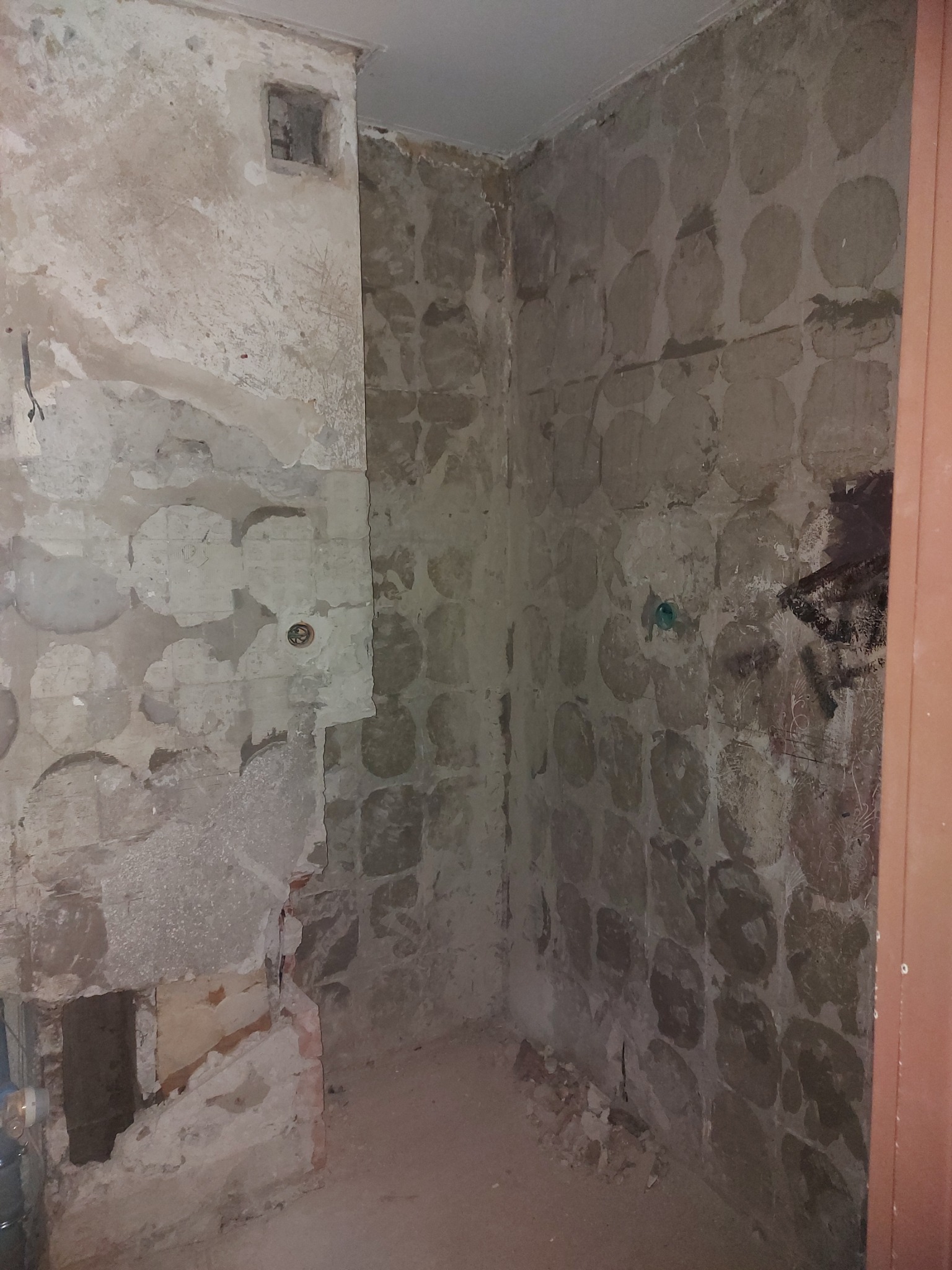 Ściany łazienki w trakcie skuwania starych płytek, odsłonięta surowa powierzchnia z pozostałościami kleju i fragmentami starej instalacji.