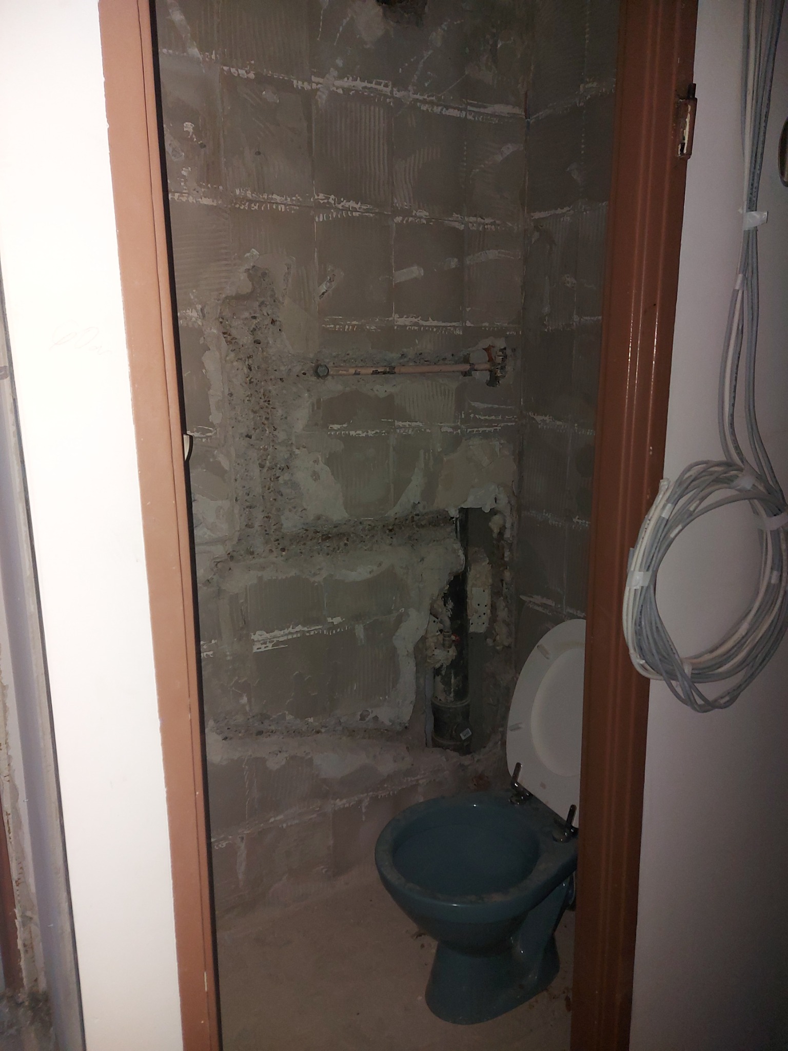 Demontaż starej toalety w trakcie prac przygotowawczych do remontu łazienki, ściany częściowo odkryte z płytek, widoczne rury instalacyjne.