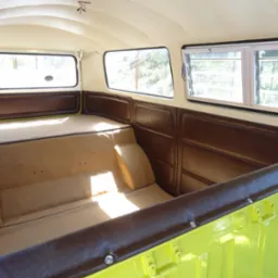 Wnętrze odrestaurowanego samochodu dostawczego typu kamper z beżową tapicerką i brązowymi panelami bocznymi, widoczne okna i jasna podsufitka.