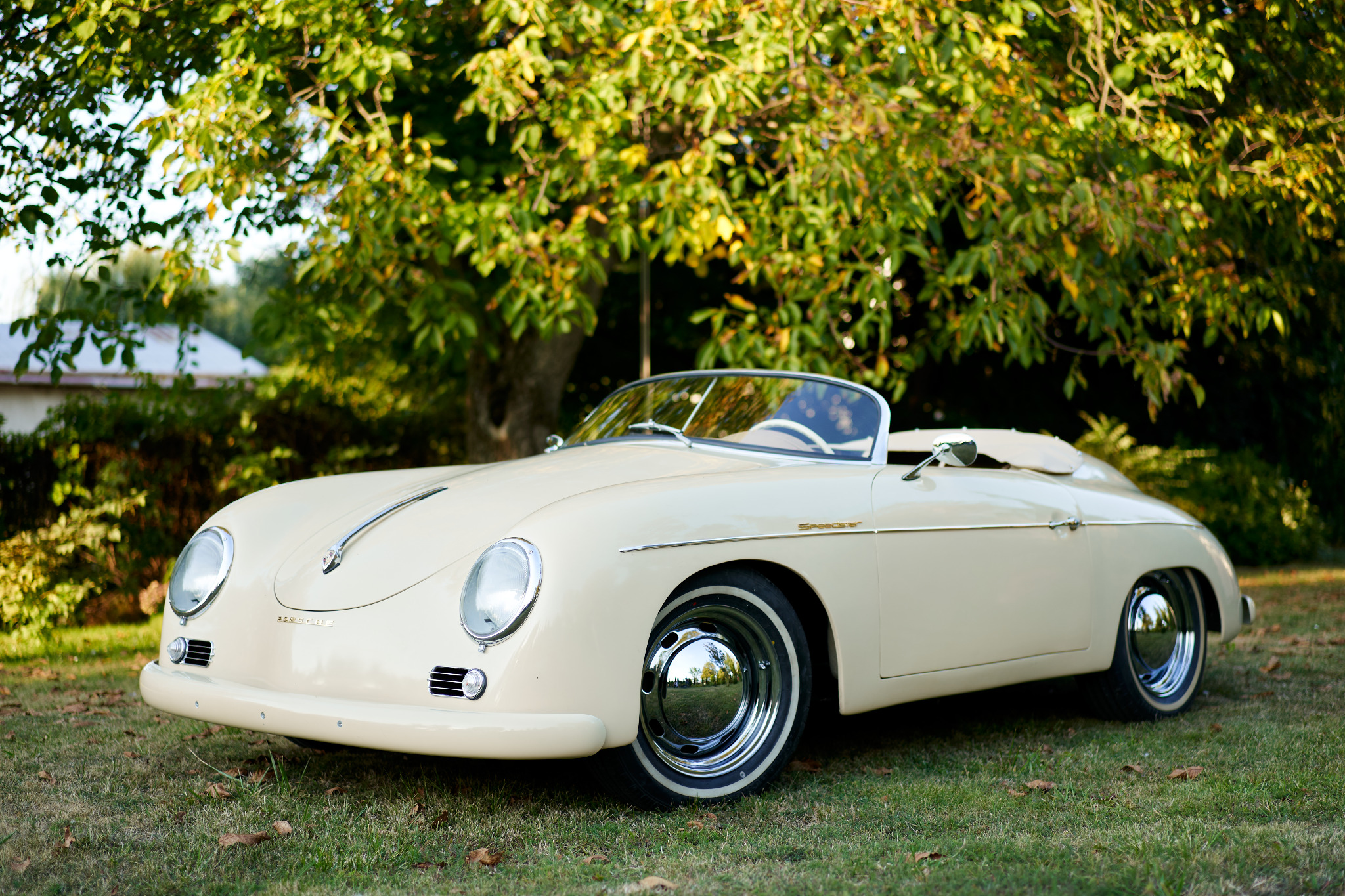 Beżowy, zabytkowy Porsche Speedster na trawie, z chromowanymi felgami i widocznym napisem 'Speedster' na błotniku.