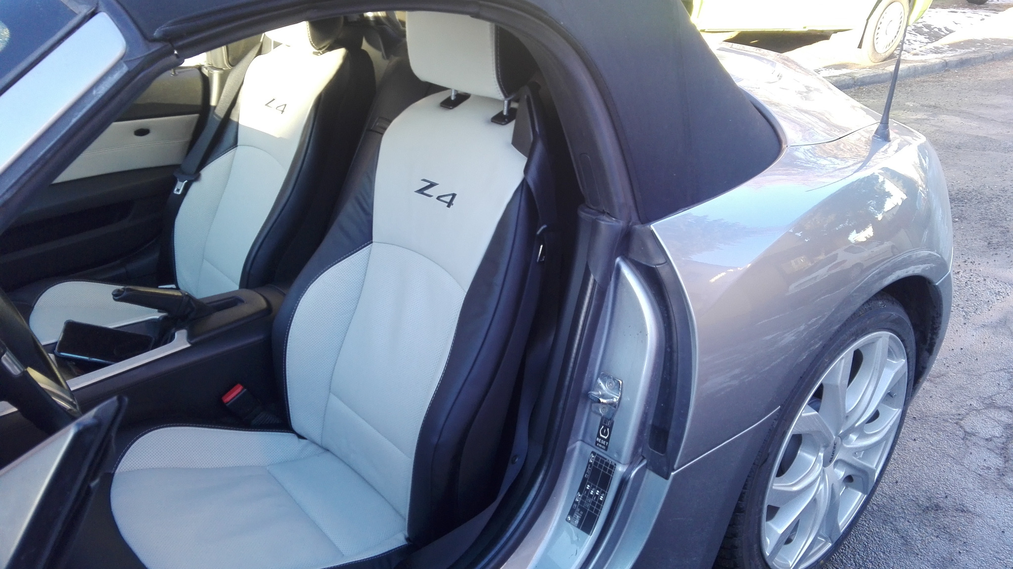 Wnętrze srebrnego BMW Z4 z jasnymi, skórzanymi fotelami z czarnymi wstawkami i logo Z4 na zagłówkach, widoczne przez otwarte drzwi.