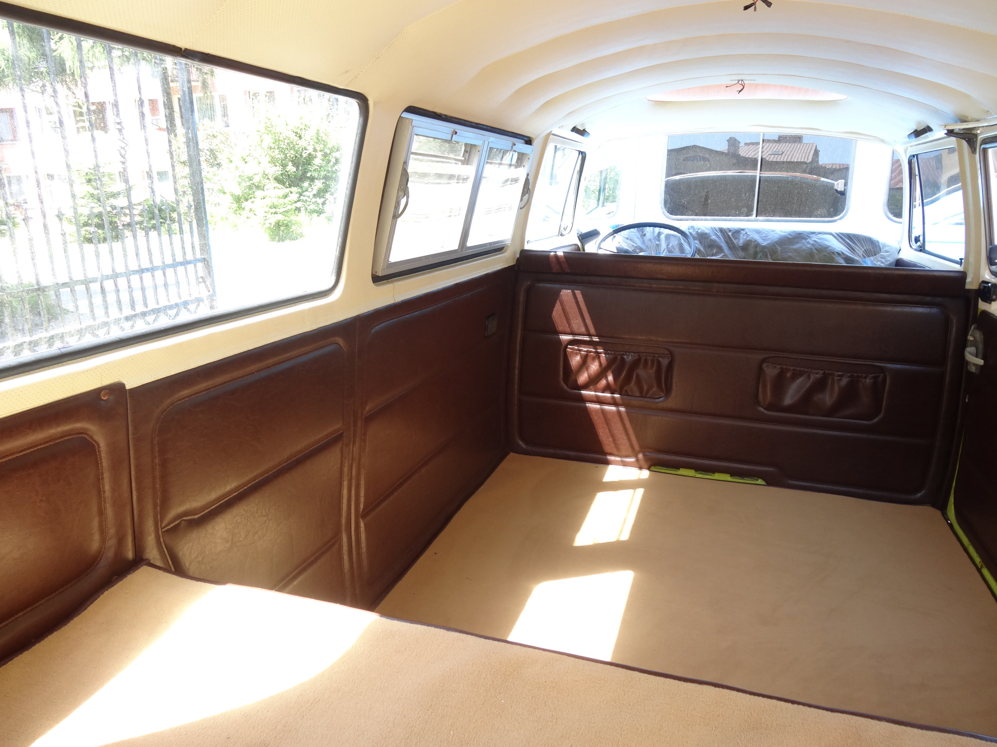 Wnętrze odrestaurowanego Volkswagena Transportera T1 z brązową tapicerką i beżową wykładziną, widoczne okna i elementy karoserii.