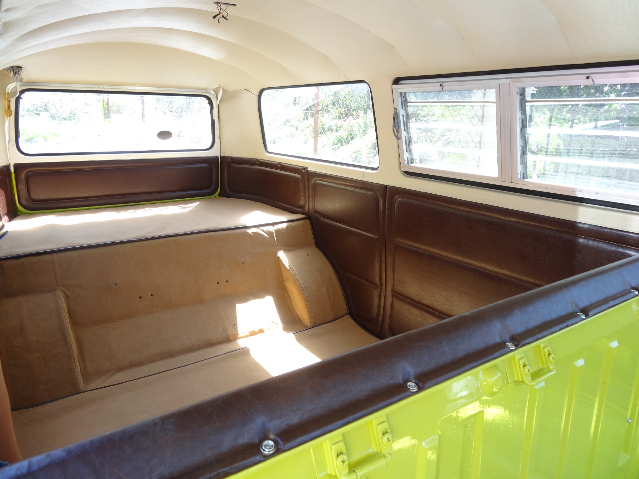 Wnętrze odrestaurowanego samochodu dostawczego typu kamper z beżową tapicerką i brązowymi panelami bocznymi, widoczne okna i jasna podsufitka.