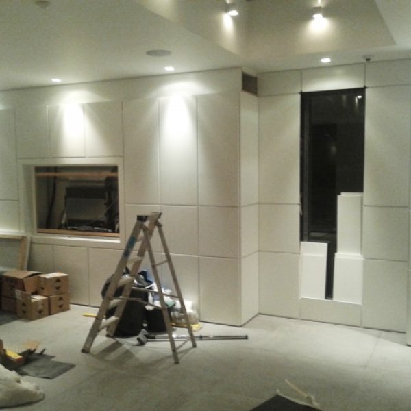 Wnętrze w trakcie prac wykończeniowych: ściany obłożone białymi panelami z widoczną drabiną, otwartym oknem i elementami konstrukcyjnymi, oświetlenie punktowe sufitowe.