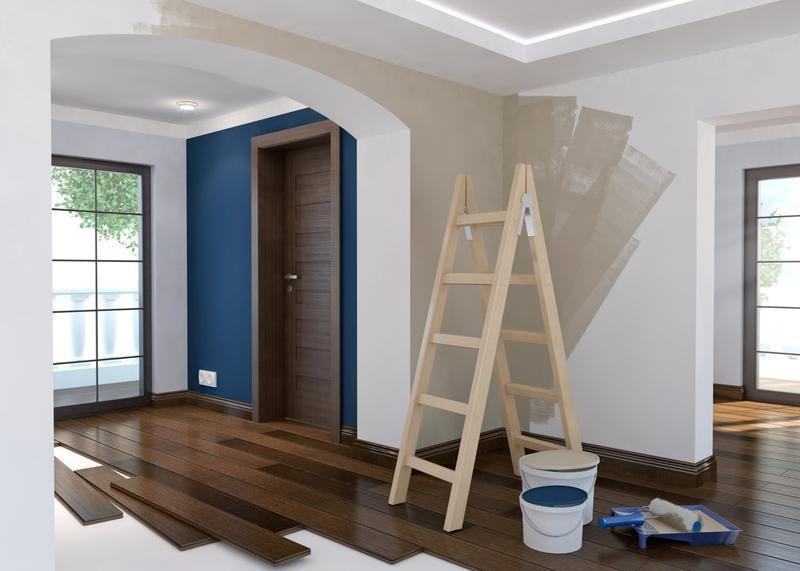 Wnętrze w trakcie odświeżania: drewniana podłoga z panelami obok, drabina oparta o ścianę z fragmentami świeżo nałożonej gładzi, dwa wiadra z farbą i kuweta z wałkiem malarskim, widok na okno...