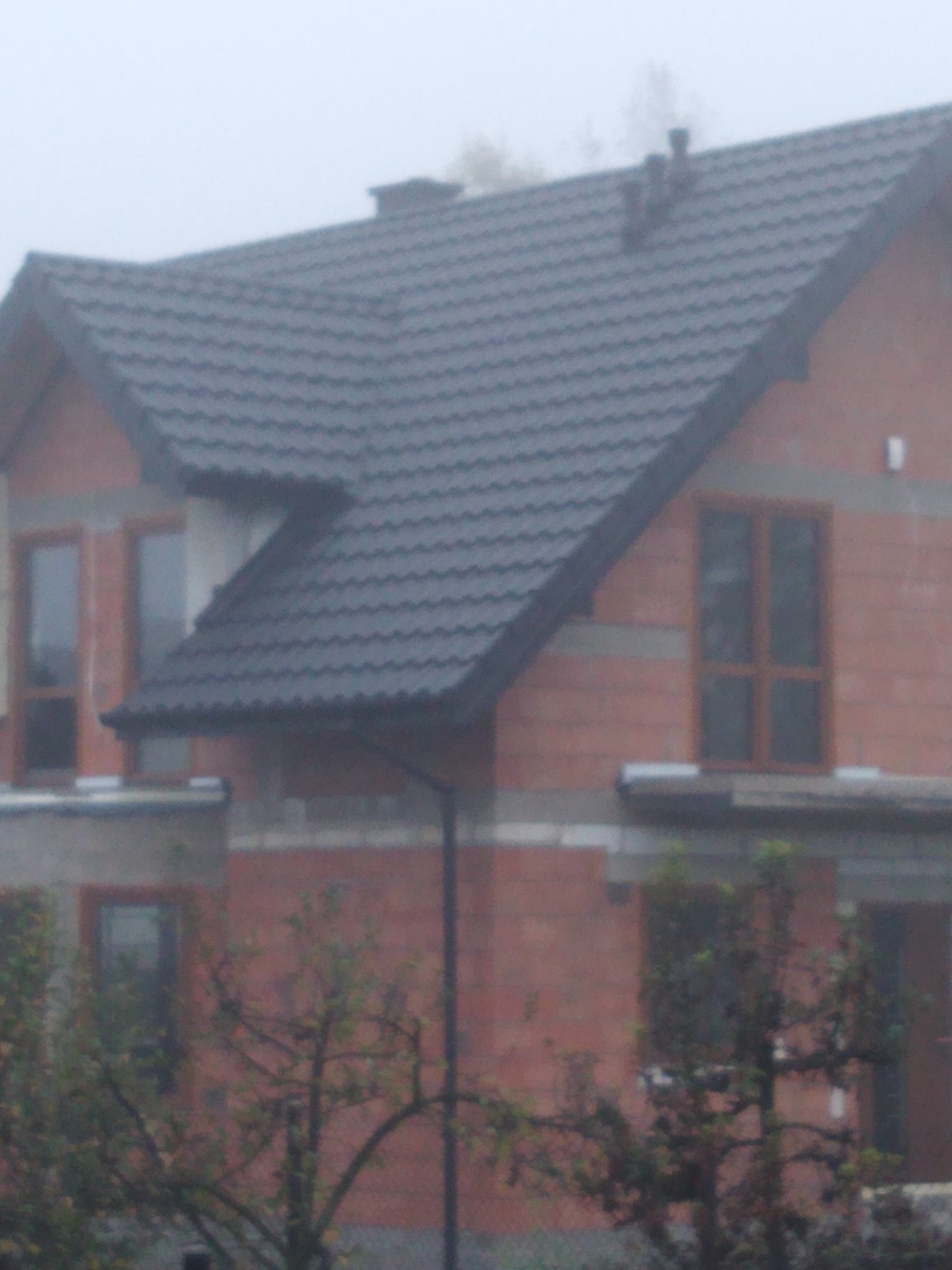 Nowy, ciemnoszary dach z blachy na dwupiętrowym domu z czerwonej cegły w mglisty dzień.