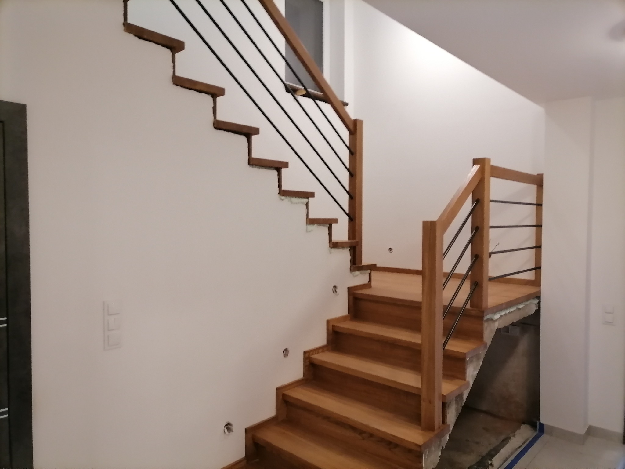 Montaż ażurowych schodów z drewnianymi stopniami i czarnymi, metalowymi balustradami w surowym stanie wykończenia wnętrza.