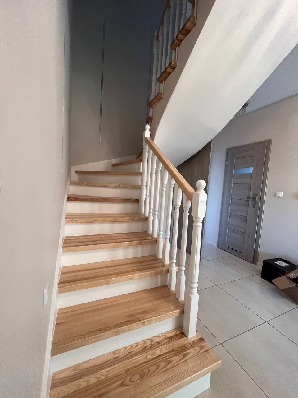 Jasne schody drewniane z białymi balustradami w nowoczesnym wnętrzu, widok z dołu ukazujący strukturę drewna stopni i minimalistyczny design.