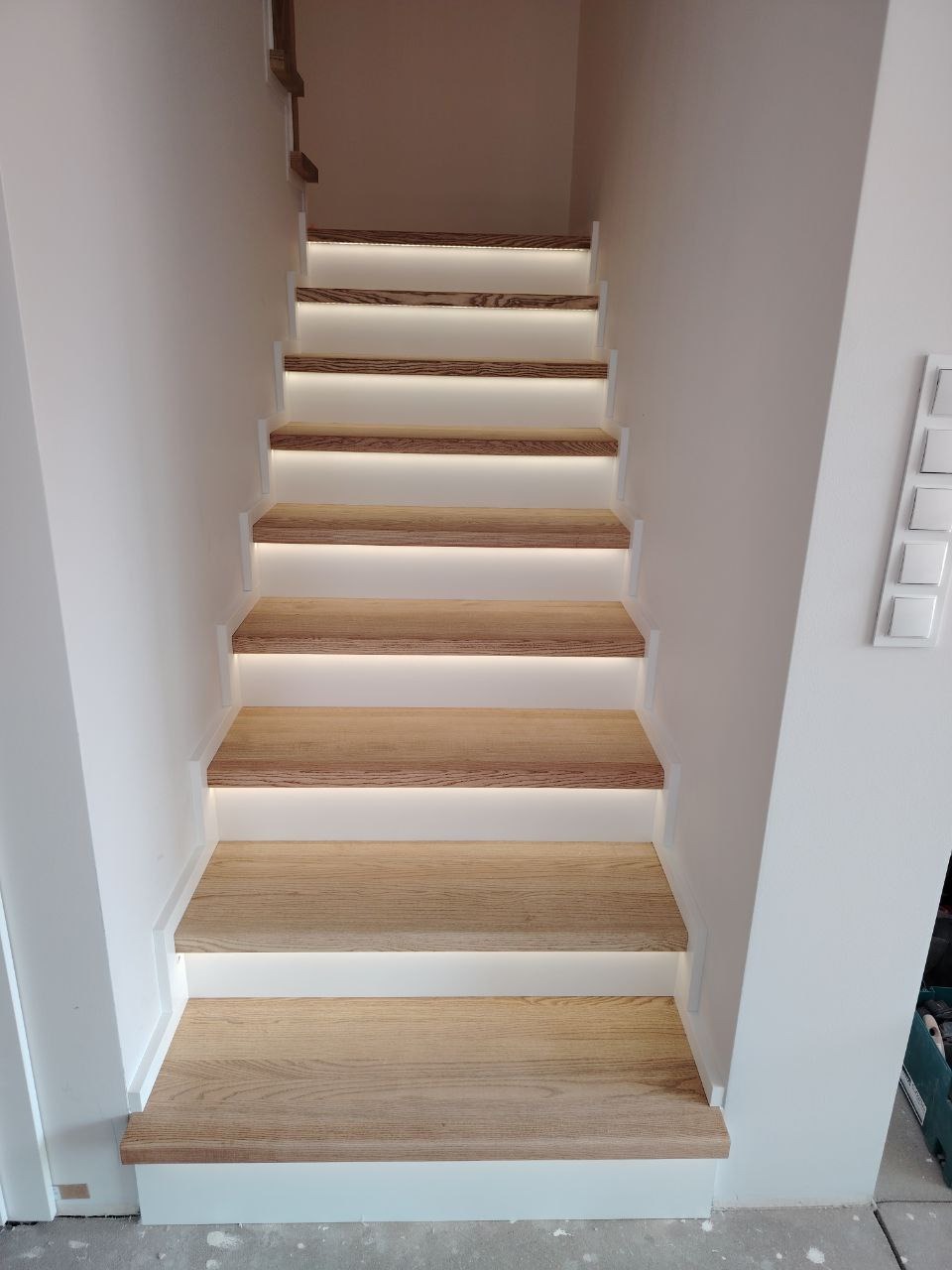Nowoczesne schody z drewna dębowego z podświetleniem LED na każdym stopniu, białe ściany, widok z dołu.