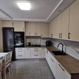 Jasna kuchnia z czarnymi akcentami: minimalistyczne szafki, blat w odcieniach brązu i marmurowe panele ścienne. Nowoczesny design z lodówką LG i stołem.