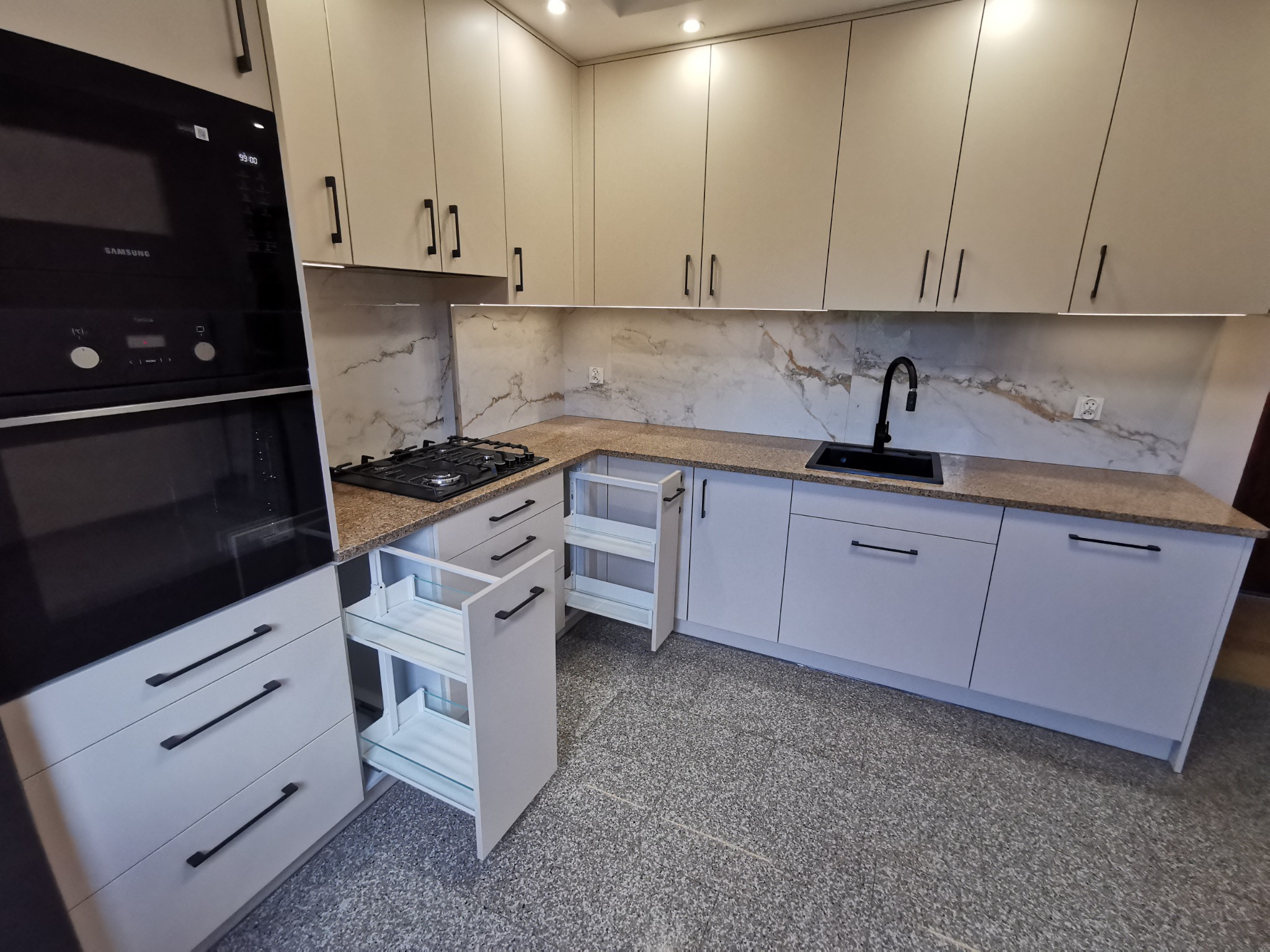 Jasna kuchnia na wymiar z czarnymi uchwytami i marmurowym backsplashiem. Wysuwane cargo w szafce narożnej. Nowoczesny design z oświetleniem LED podszafkowym.