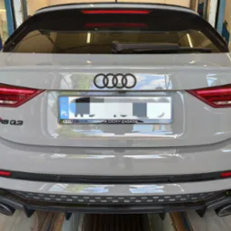 Tył szarego samochodu Audi RS Q3 w warsztacie, widoczne logo Audi, tablica rejestracyjna i dyfuzor z końcówkami wydechu.
