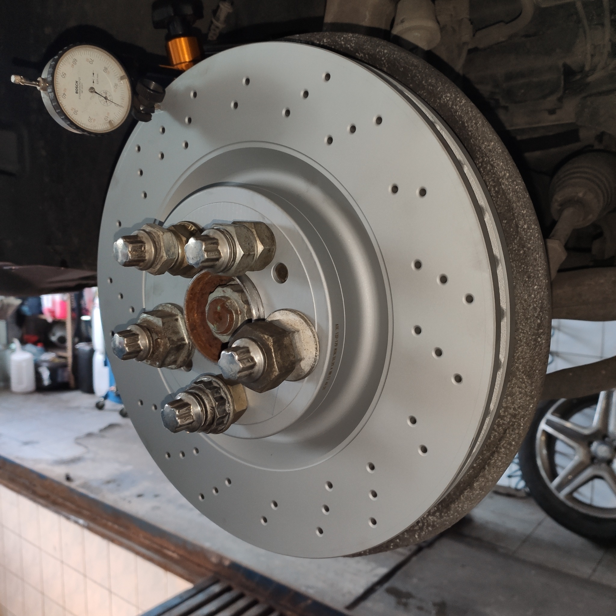 Nowa, nawiercana tarcza hamulcowa zamontowana w samochodzie, sprawdzana czujnikiem zegarowym Bosch. Widoczne ślady korozji na śrubach mocujących.
