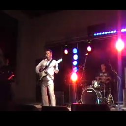 Arawak Krzysztof Boguń - Zespół muzyczny grający na scenie podczas koncertu, wokalista z gitarą na pierwszym planie, perkusista w tle, oświetlenie sceniczne.