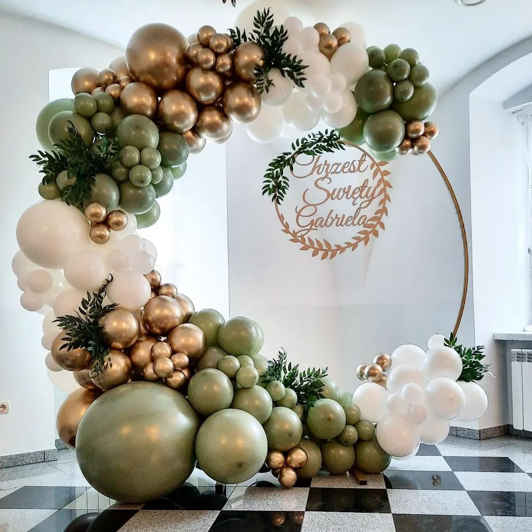 Okrągła dekoracja balonowa w odcieniach zieleni, złota i bieli z napisem 'Chrzest Święty Gabriela' na tle białej ściany i czarno-białej podłogi.
