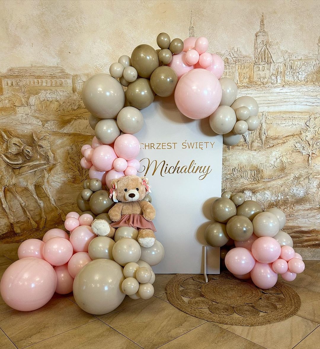 Dekoracja balonowa w odcieniach różu i beżu z pluszowym misiem na tle tablicy z napisem 'Chrzest Święty Michaliny', na podłodze okrągły dywanik.