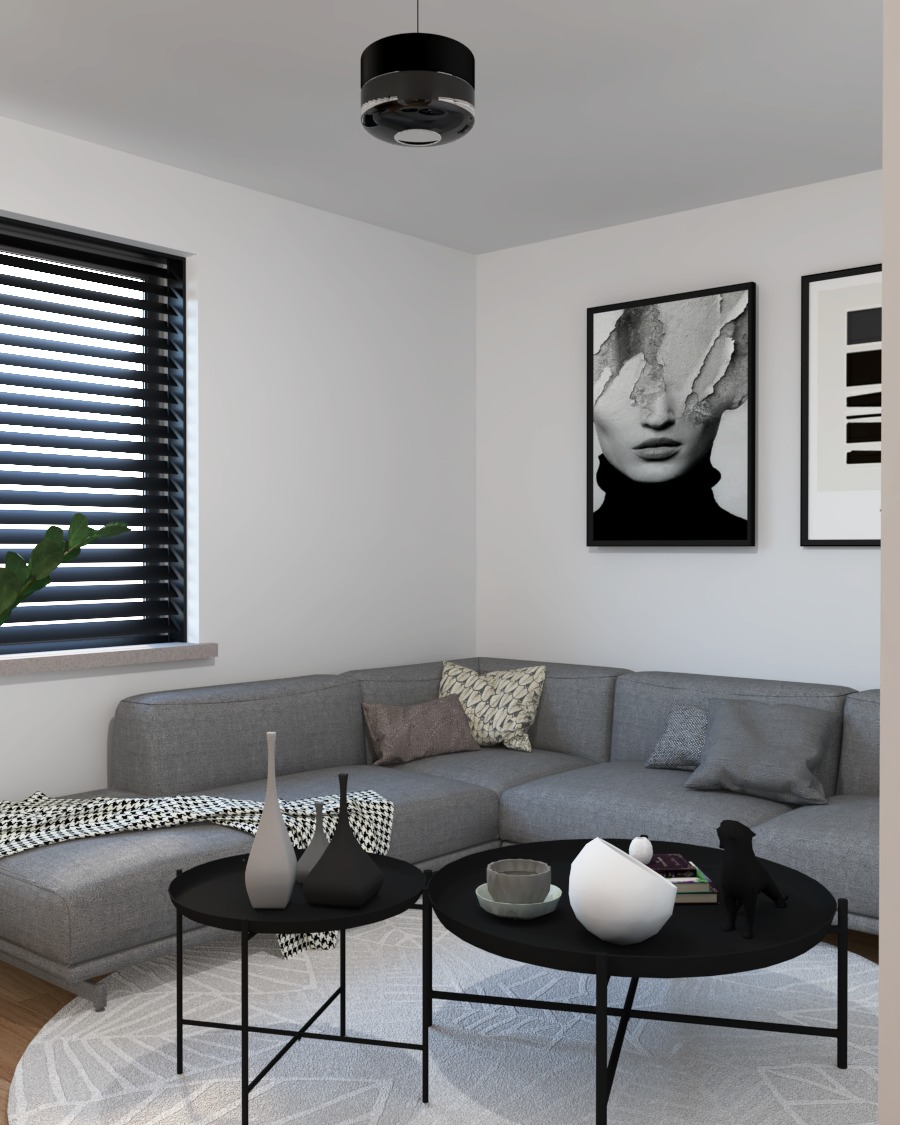 Szary narożnik z poduszkami w salonie, dwa czarne stoliki kawowe z dekoracjami, grafiki na ścianie i rolety w oknie.