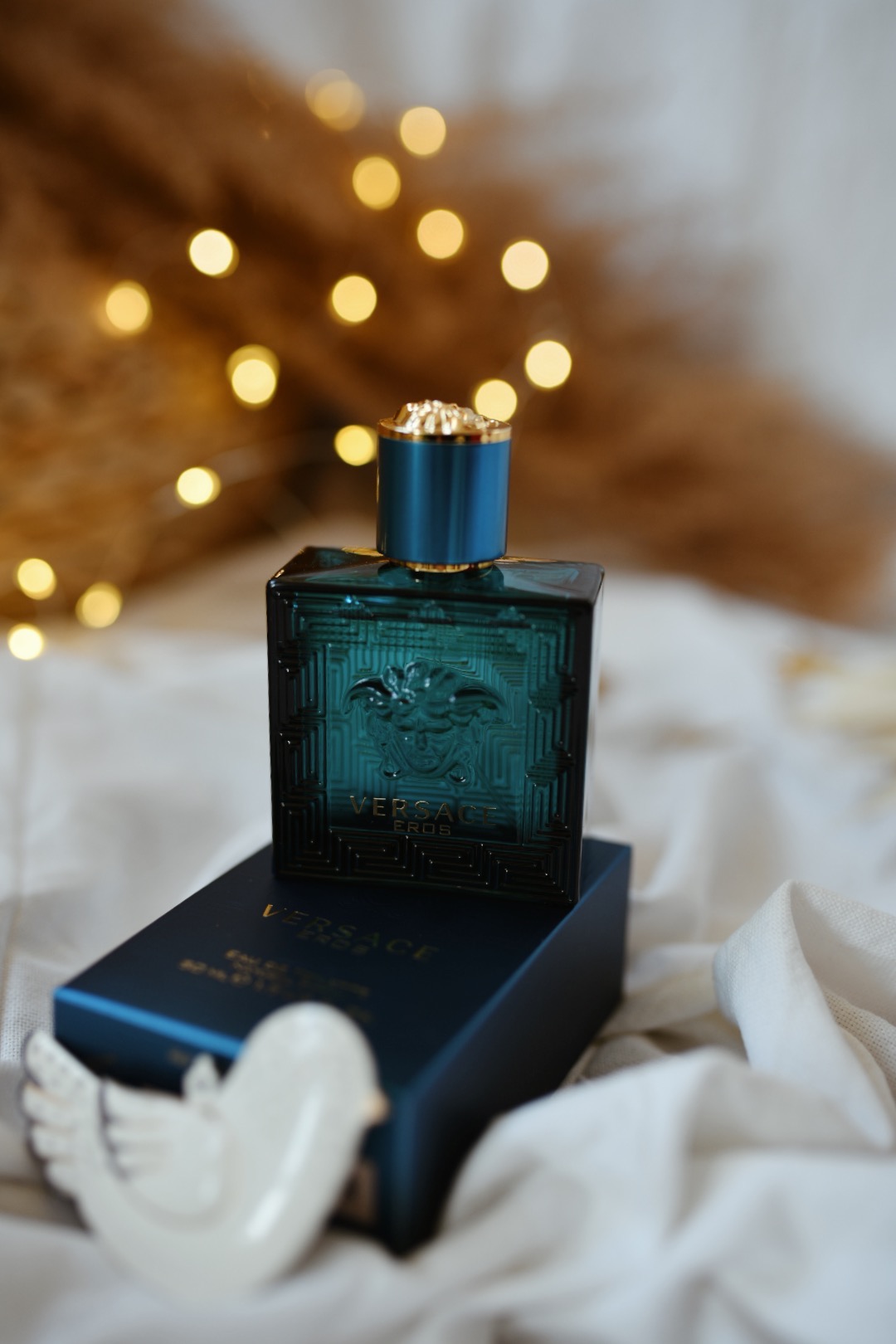 Flakon perfum Versace Eros na pudełku, dekorowany ceramiczną figurką ptaszka, w tle rozmyte światełka, prezentowany przez firmę z Łodzi.