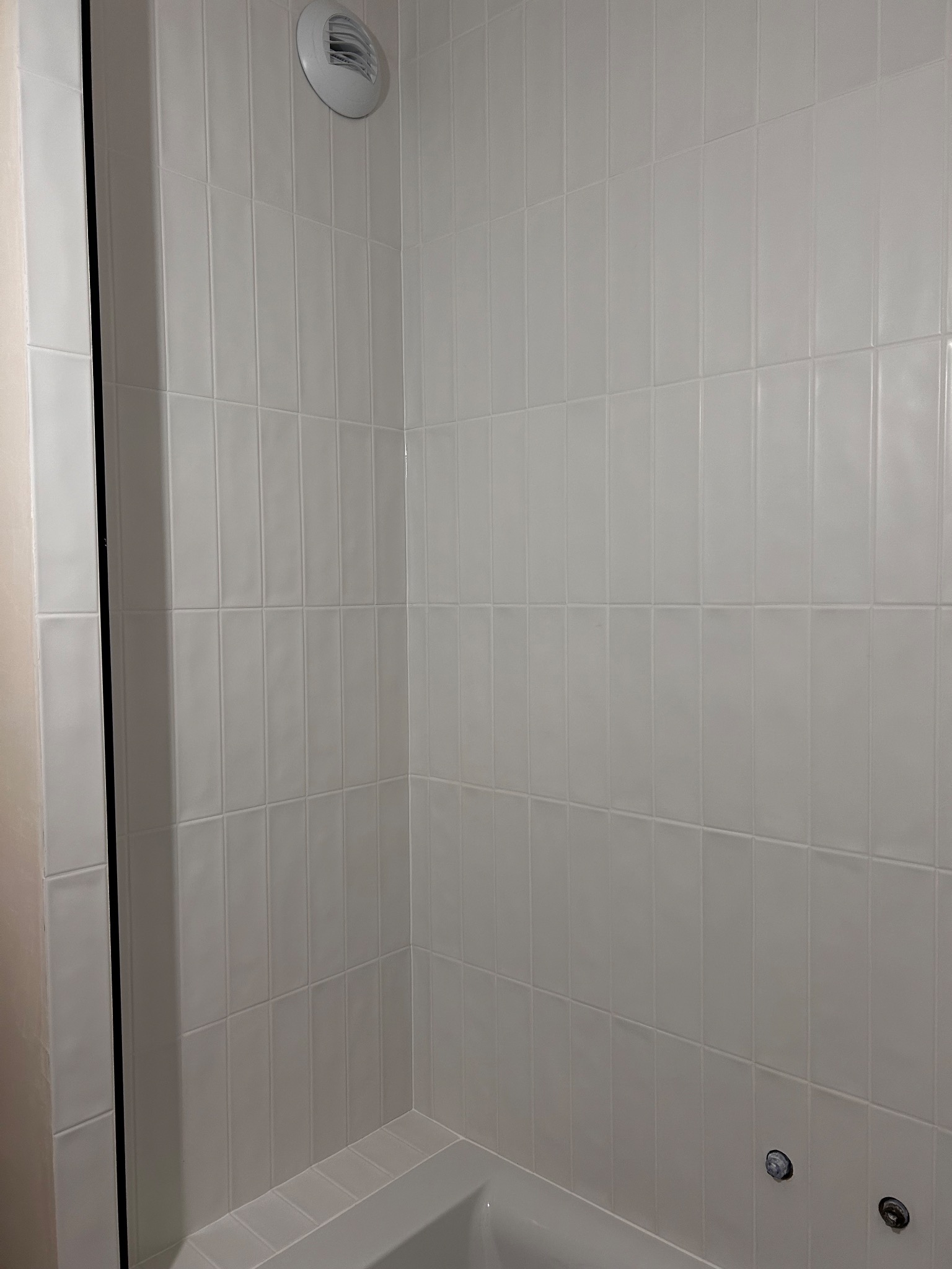 Wnętrze wykończonej łazienki z białymi, pionowo ułożonymi płytkami, widoczny fragment wanny i okrągły nawiewnik wentylacyjny w górnym rogu.