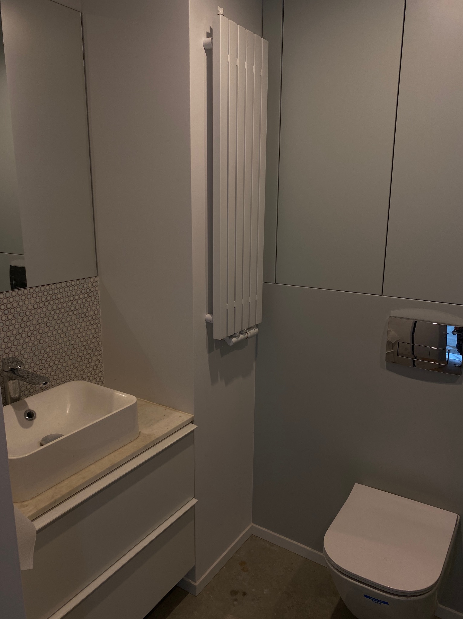Nowoczesna łazienka w odcieniach szarości z wiszącą toaletą, umywalką nablatową i grzejnikiem drabinkowym.