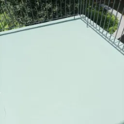 Jasny, pomalowany na zielono balkon z metalową barierką, widok z góry na gęste drzewa w tle.