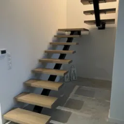 Nowoczesne schody wspornikowe z drewnianymi stopniami i czarną metalową konstrukcją, oświetlone ciepłym światłem, z dekoracyjnymi lampionami w tle.