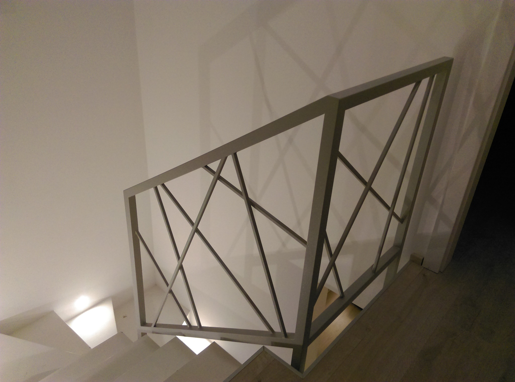 Metalowa balustrada schodowa z geometrycznym wzorem, pomalowana na szaro, widoczna z góry, z elementami spawania w narożnikach.