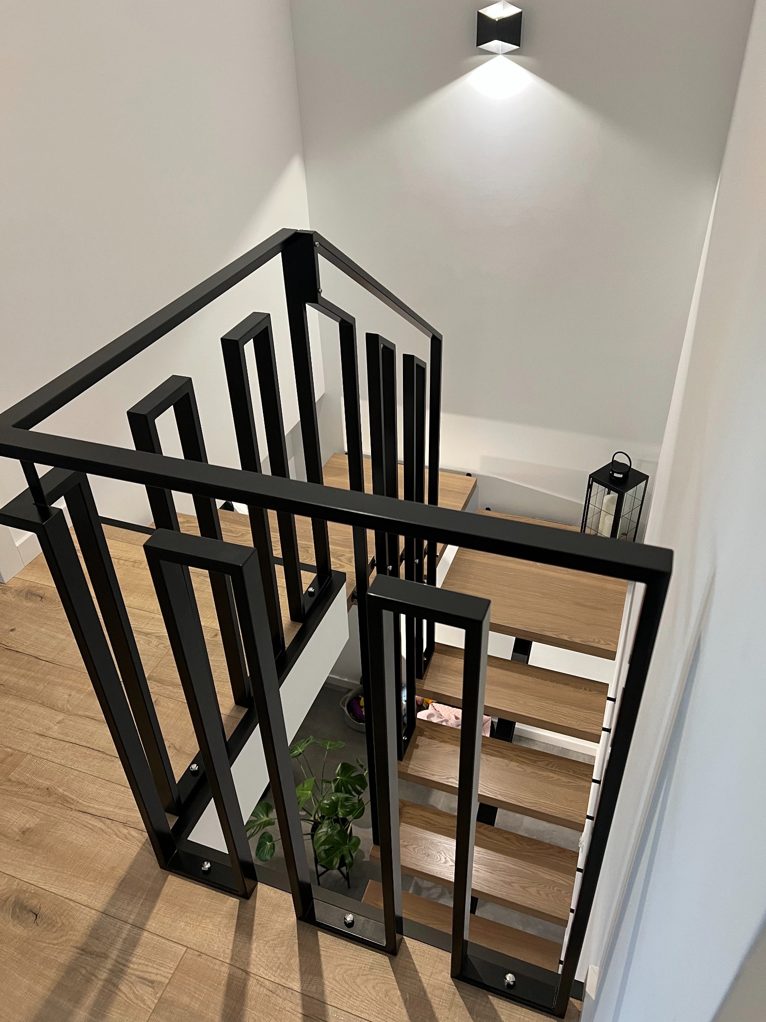 Nowoczesna, czarna balustrada schodowa o geometrycznym wzorze w domu w Otominie, widok z góry na drewniane schody i białe ściany.