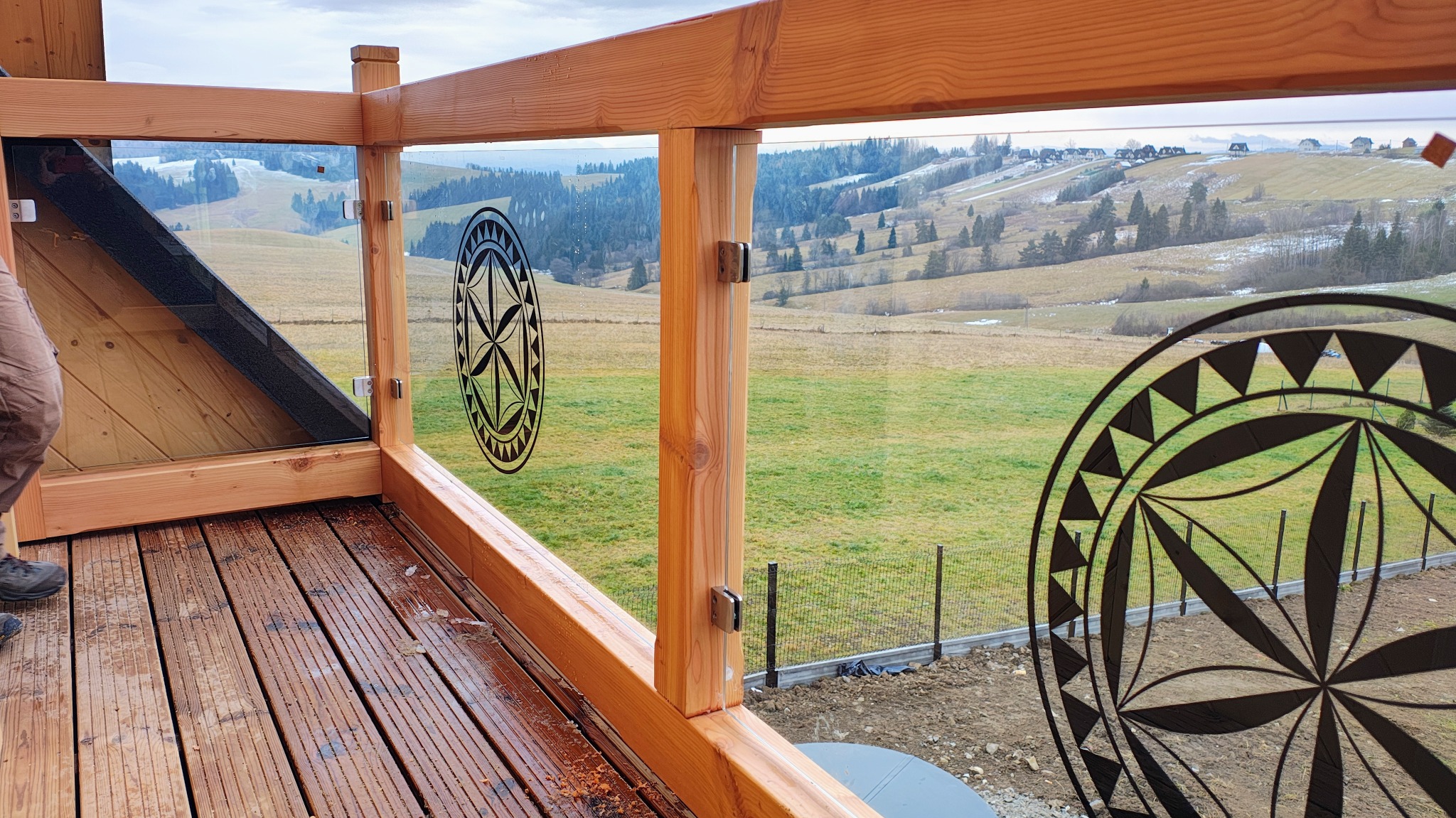 Drewniany balkon z balustradą ze szkła hartowanego z motywem regionalnym, widok na pagórkowaty krajobraz