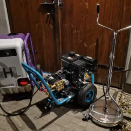 Profesjonalny sprzęt do mycia ciśnieniowego: myjka Falch i urządzenie do czyszczenia powierzchni Turbo Devil, gotowe do pracy na tle drewnianej bramy.