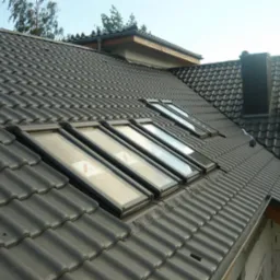 Czarny dach z dachówki ceramicznej z zamontowanymi oknami dachowymi, widok z góry na budynek w trakcie budowy.