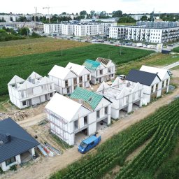 JKBuilding - Domy w trakcie budowy z betonu komórkowego, widok z drona. Jeden dom z czarnym dachem ukończony, pozostałe w stanie surowym otwartym, z elementami więźby dachowej.