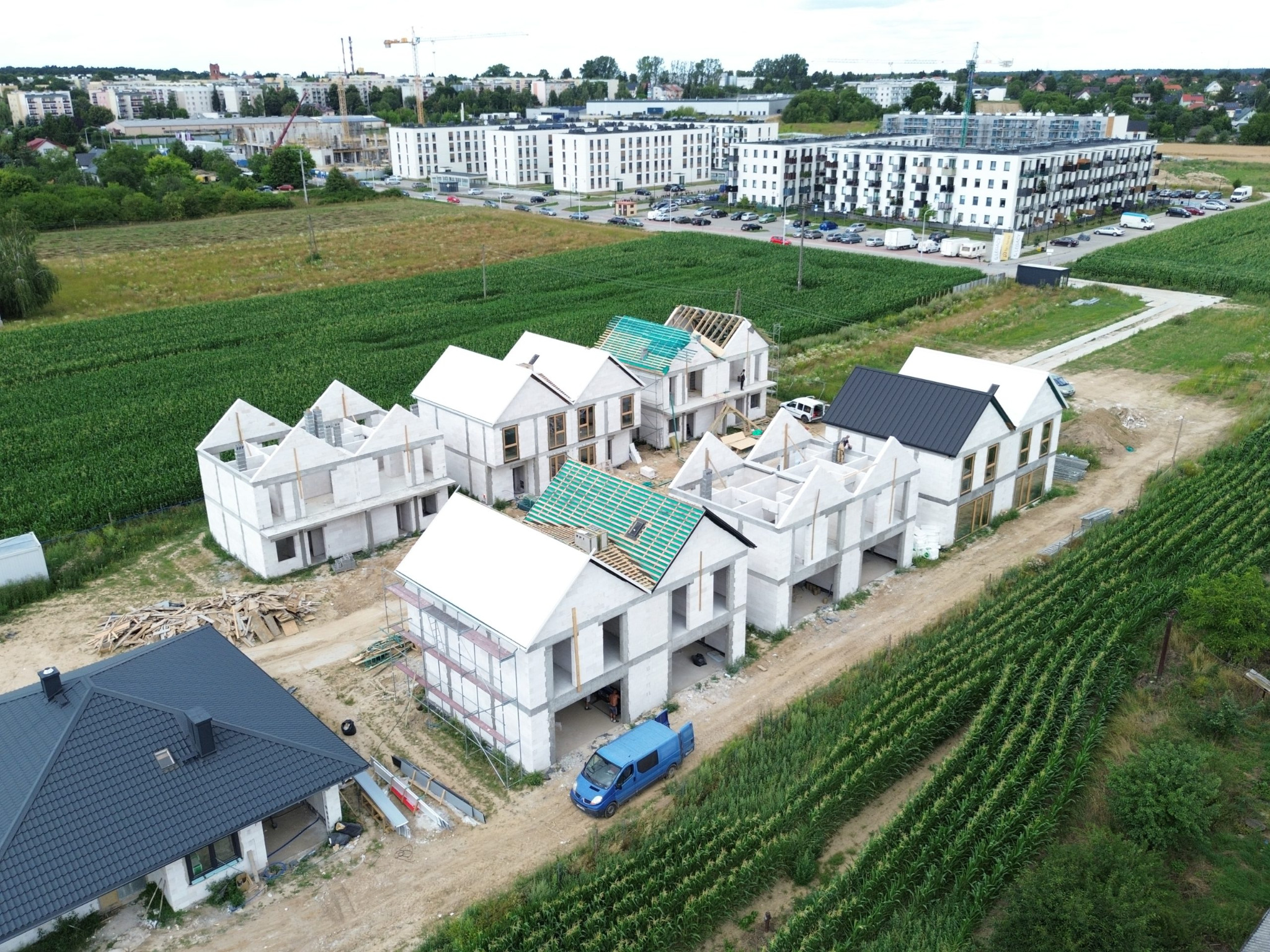 Domy w trakcie budowy z betonu komórkowego, widok z drona. Jeden dom z czarnym dachem ukończony, pozostałe w stanie surowym otwartym, z elementami więźby dachowej.