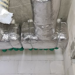 Instal-Grzew Grzegorz Salamon - Izolowane przewody wentylacyjne pod sufitem z betonu komórkowego, zabezpieczone metalowymi taśmami.