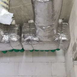 Izolowane przewody wentylacyjne pod sufitem z betonu komórkowego, zabezpieczone metalowymi taśmami.