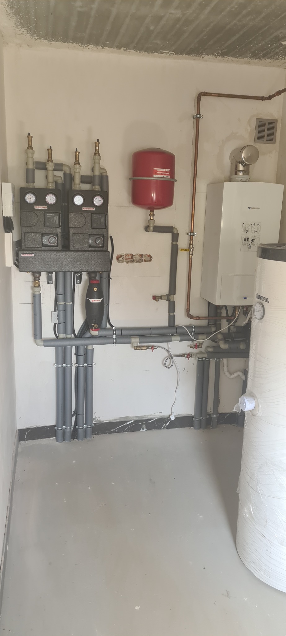 Kompleksowa instalacja grzewcza z kotłem Junkers, zasobnikiem Kospel i rozdzielaczami DePro w kotłowni w Połomi, widoczne rury i osprzęt.